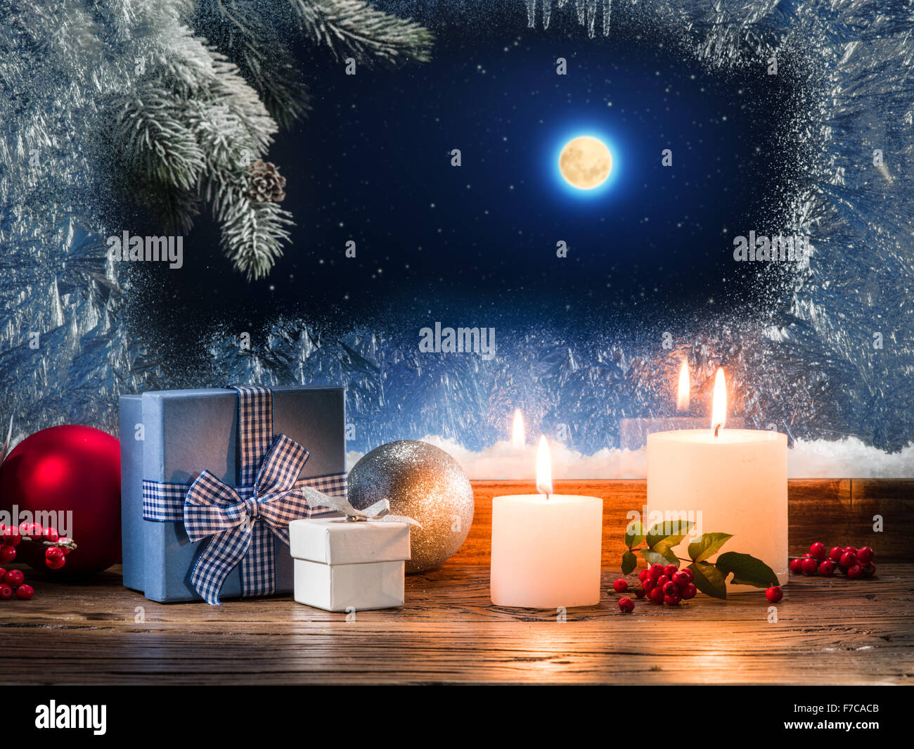 Christmas presents with burning candle on the windowsill with pattern frost. Stock Photo