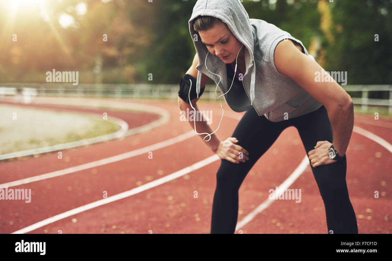 Young sportswoman standing on stadium and listening to music, looking down Stock Photo