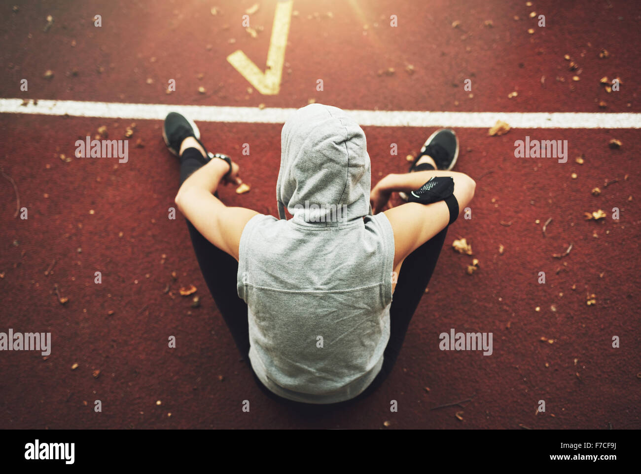 Back view of young woman in sportswear sitting on track field and preparing before training.Unrecognizable Stock Photo