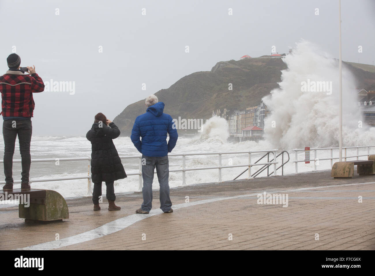 Aberystwyth, Wales, UK. 29th November 2015 Three pedestrians watch and take photos as the big waves batter Aberystwyth this morning as storm Clodagh combines with high tide. Credit:  Ian Jones/Alamy Live News Stock Photo