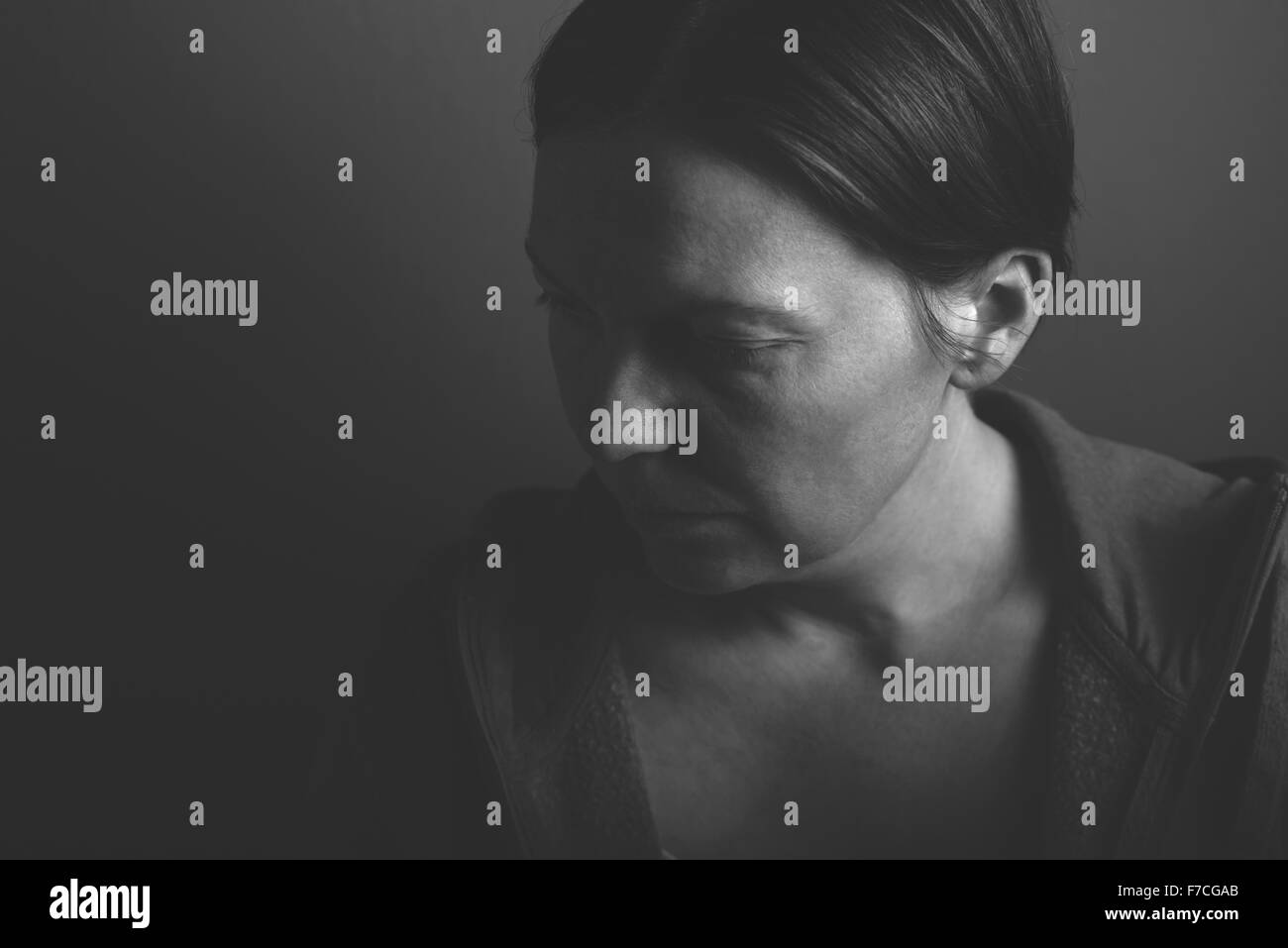 Depressive woman, low key monochromatic portrait of sad adult female in dark room Stock Photo