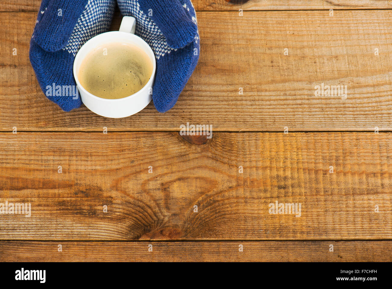 Woman hands in teal gloves are holding a mug with hot coffee or cocoa ...