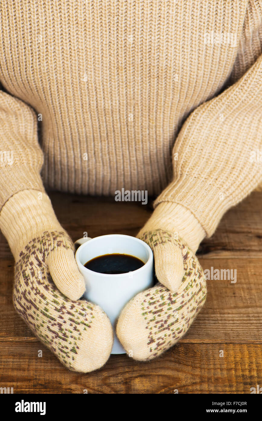 Woman hands in teal gloves are holding a mug with hot coffee or cocoa ...
