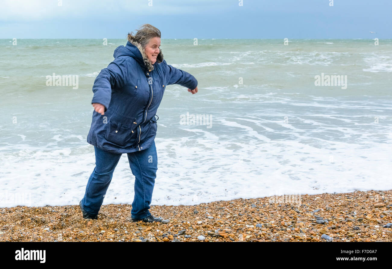 Middle aged woman on a beach running from waves in the UK. Stock Photo