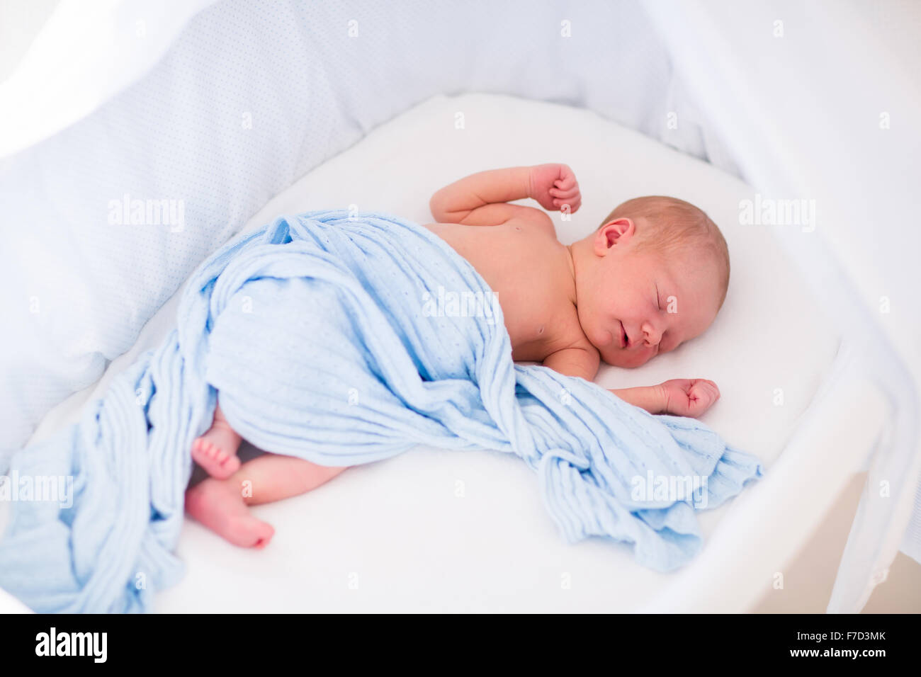 Newborn baby boy waking up on a sunny morning in white bed. New born