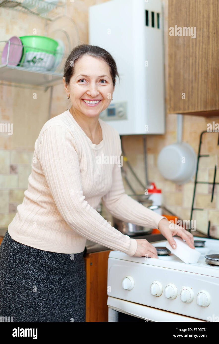 Happy mature housewife cleans the gas-stove  with sponge Stock Photo