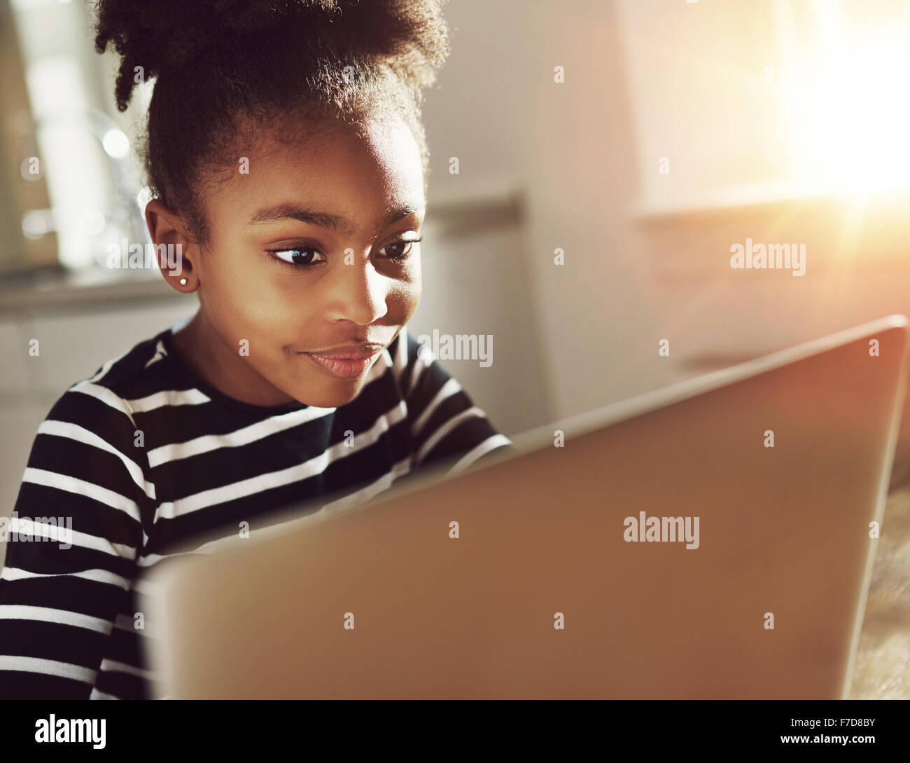 Smiling black girl using a laptop at home sitting reading information ...