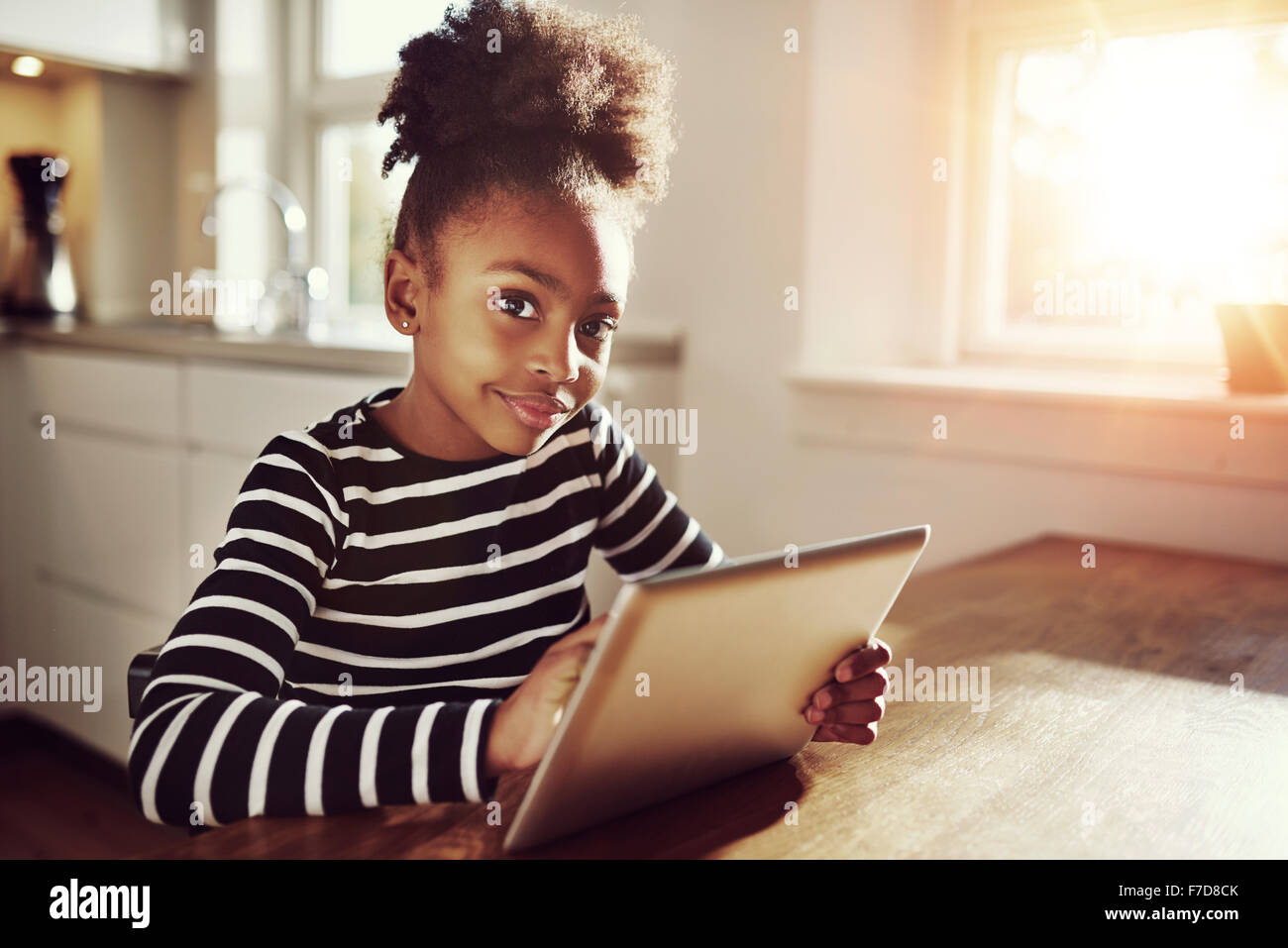 Thoughtful young black girl sitting watching the camera with a pensive expression as she browses the internet on a tablet comput Stock Photo