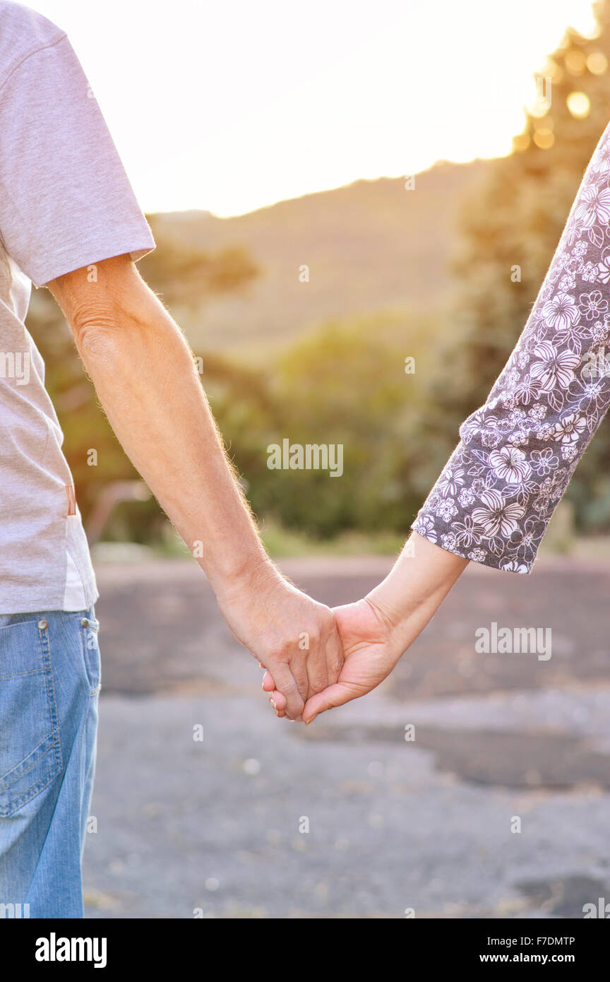 Couple holding hands in the park facing sunset Stock Photo