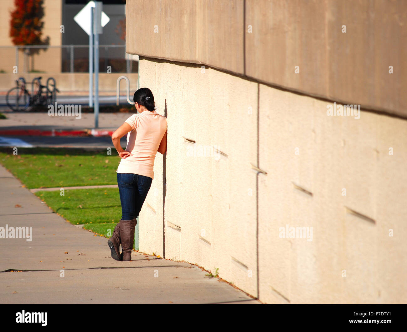 Woman in tight jeans and boots looking at her phone as she stands alongside a cement wall. Stock Photo