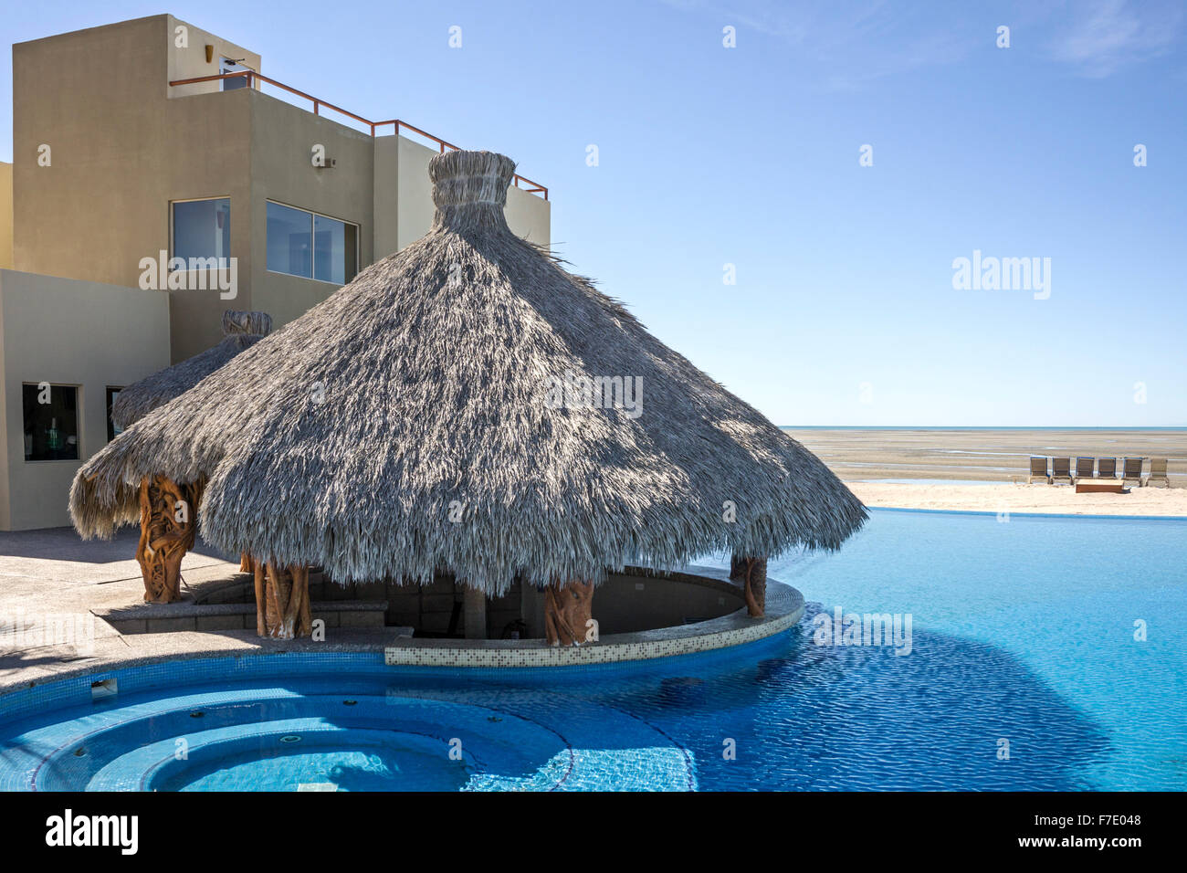 palapa awaits bar equipment to serve swimmers in unreal blue infinity pool overlooking wide beach stretching far out at low tide Stock Photo