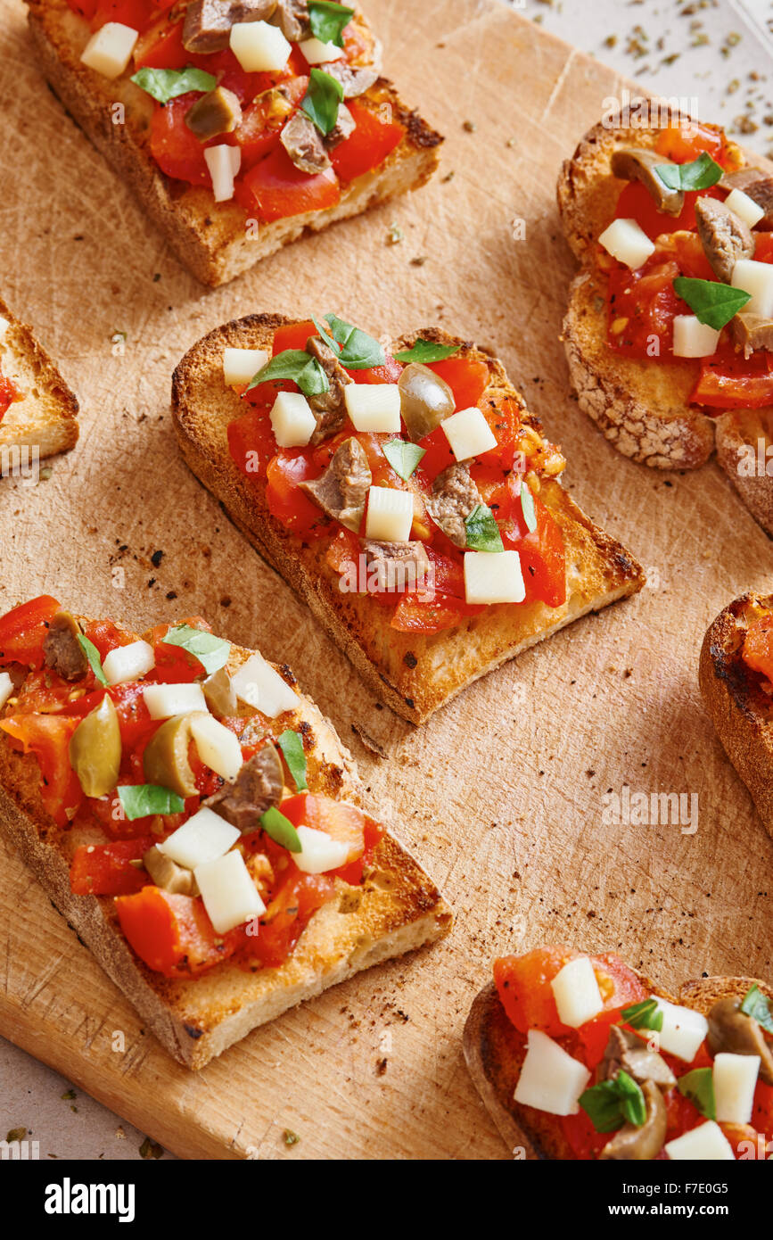 Bruschetta tomato, cheese, olives and garlic on cutting board and wooden table surrounded by tomato and garlic Stock Photo