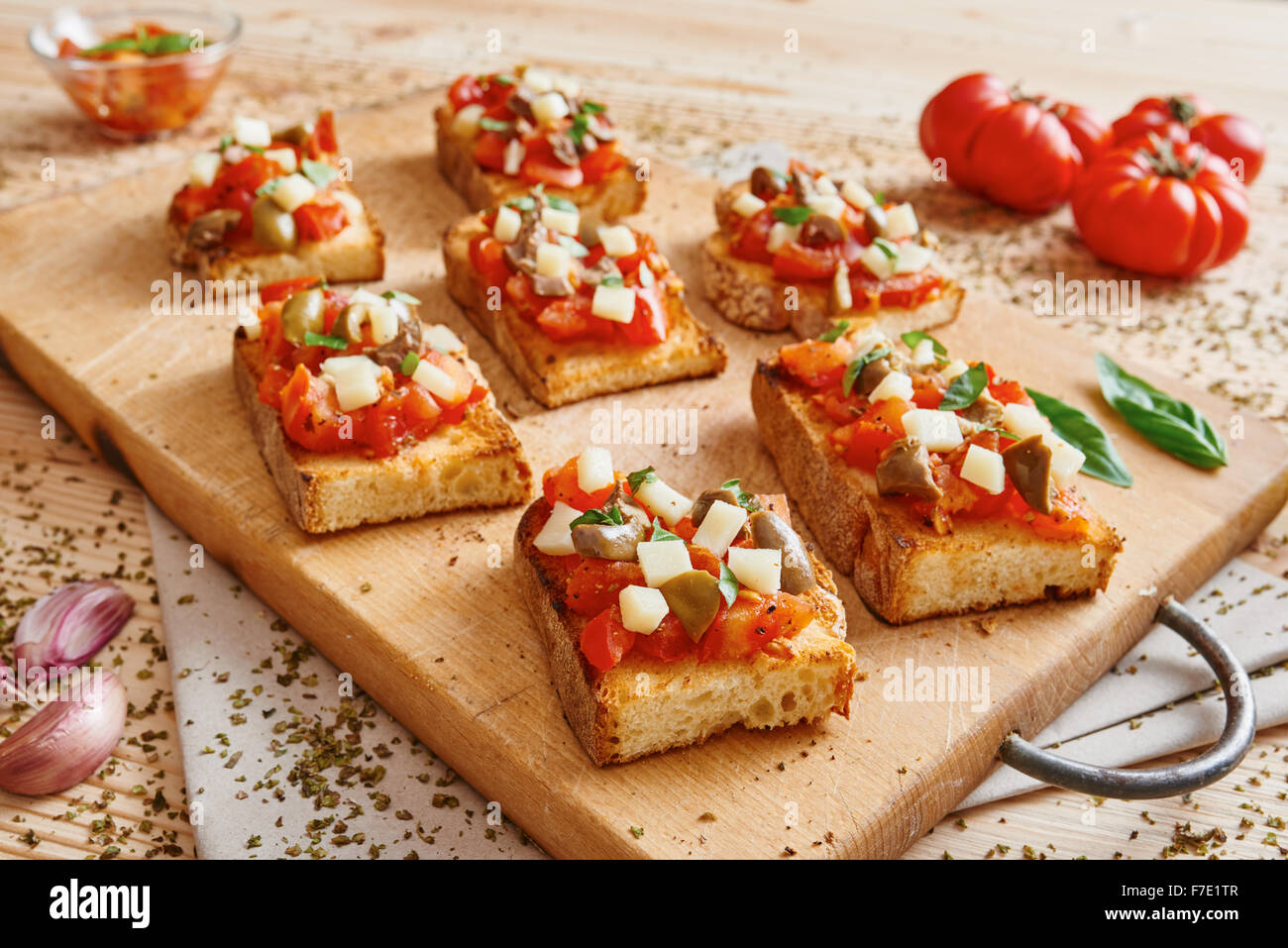 Bruschetta tomato, cheese, olives and garlic on cutting board and wooden table surrounded by tomato and garlic Stock Photo