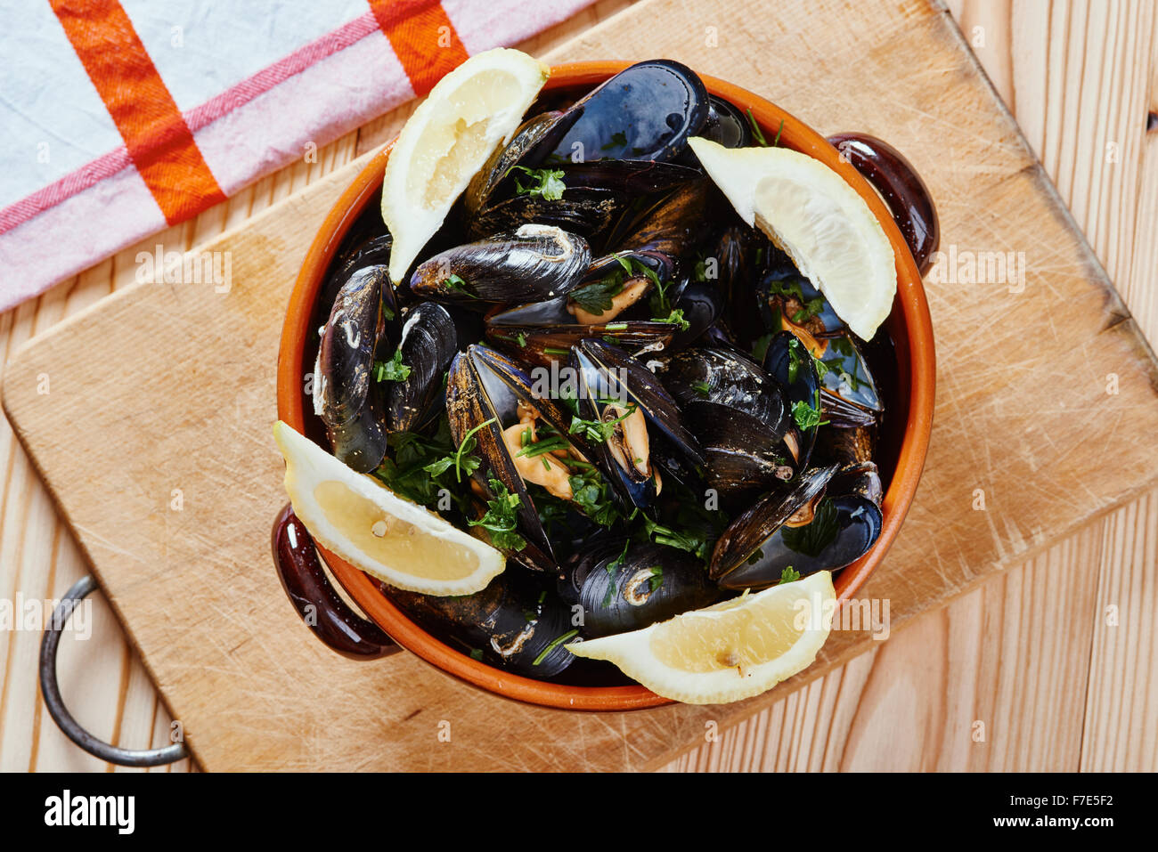 Mussels in a pot on the cutting board, lemons, tablecloth on wooden table Stock Photo