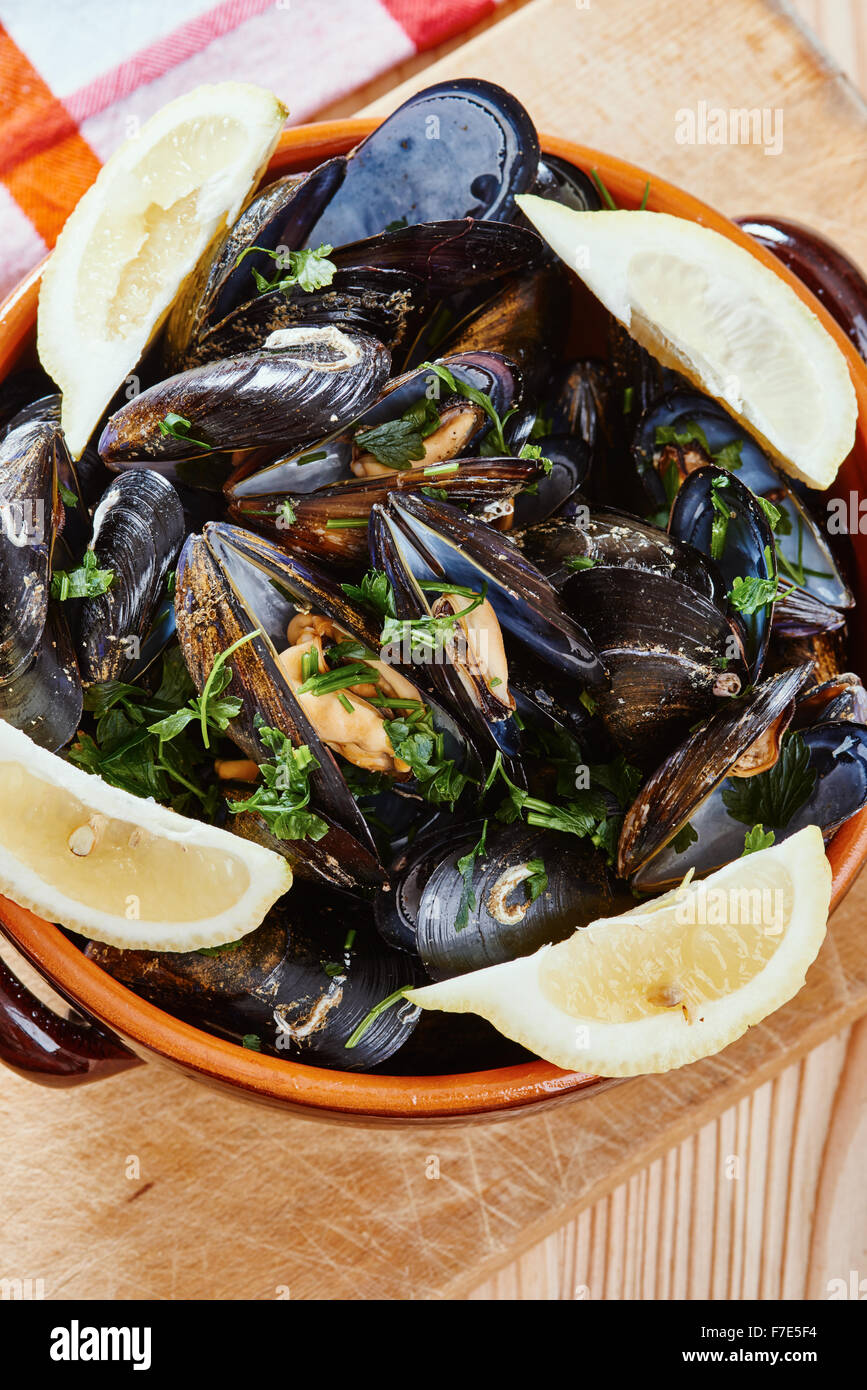 Mussels in a pot on the cutting board, lemons, tablecloth on wooden table Stock Photo