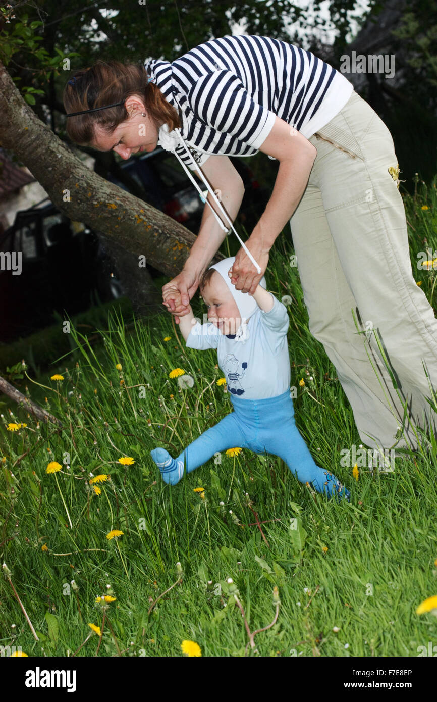 One year old baby learning to walk by holding his mother's hands Stock