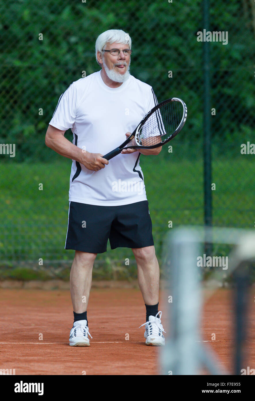 Senior man playing tennis on a gravel court Stock Photo