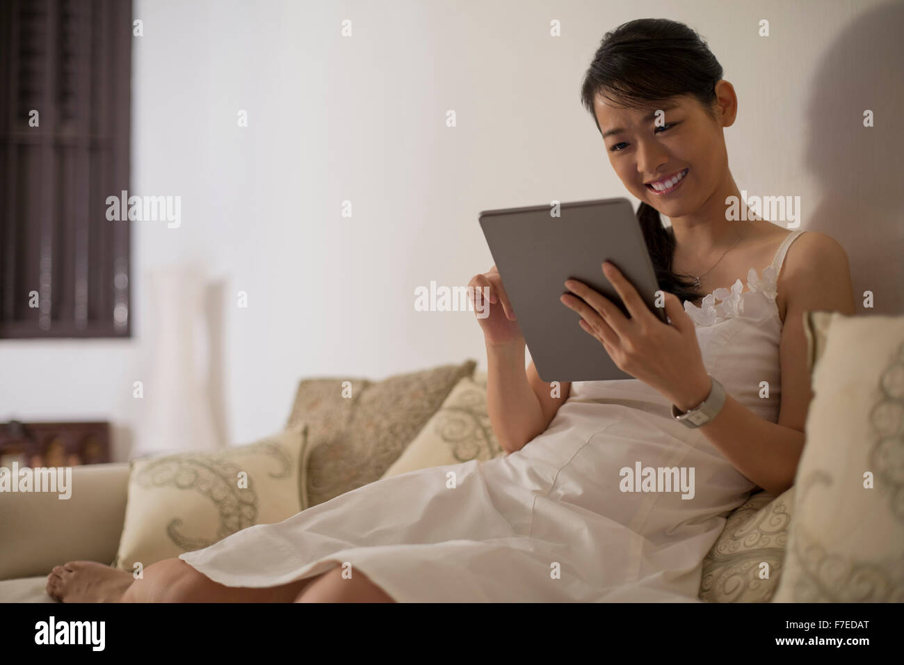 Singapore, Woman sitting on sofa using digital tablet Stock Photo - Alamy