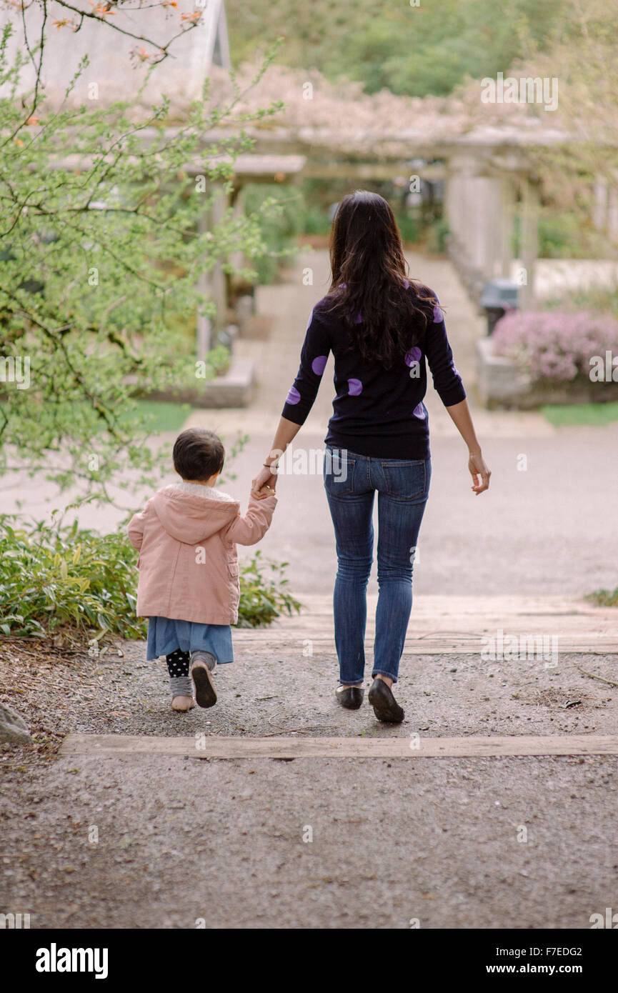 USA, Rear view of mother and daughter (2-3) holding hands in park Stock Photo