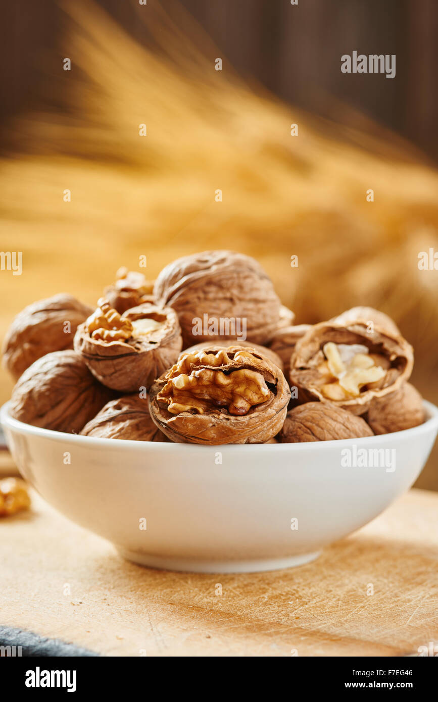 Walnuts on white bowl resting on a cutting board and wooden table Stock Photo