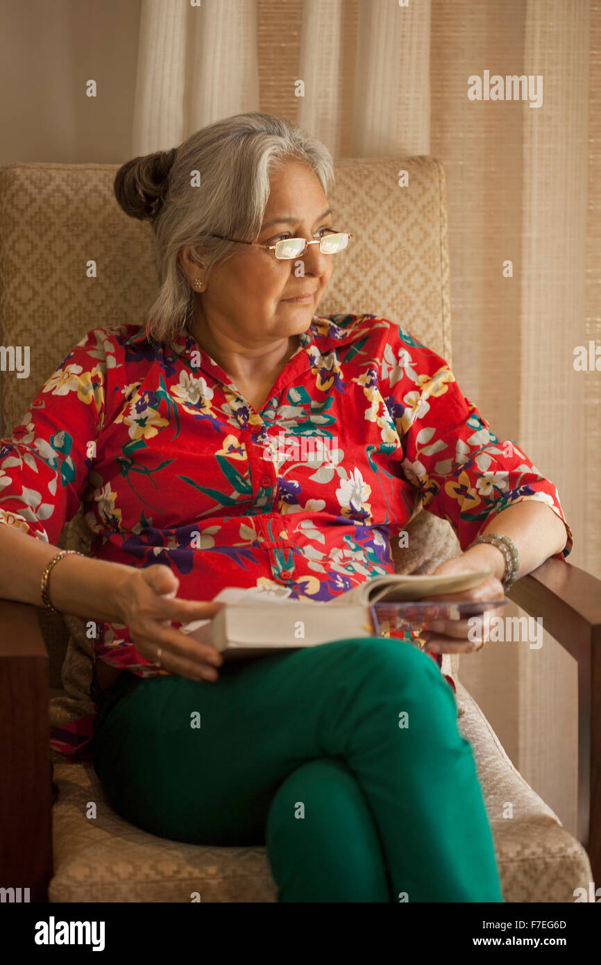 India, Senior woman sitting in armchair reading book Stock Photo - Alamy