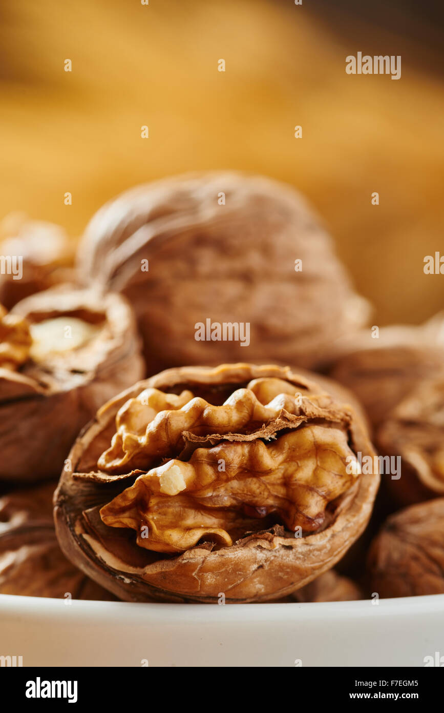 Walnuts on white bowl resting on a cutting board and wooden table Stock Photo