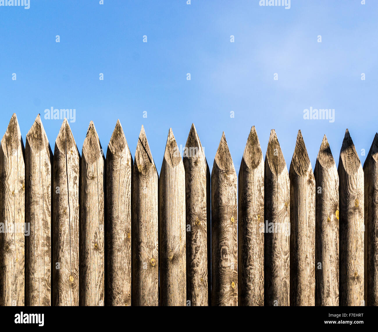 Rustic wooden palisade fencing forming a defensive barrier against a blue sky background Stock Photo