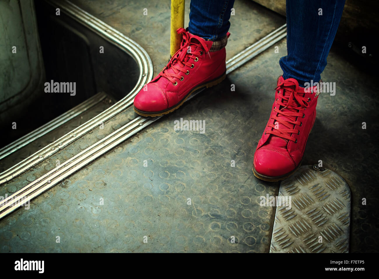 Unknown human feet wearing bright red boots on a public bus with a grunge style dirty background with a copy-space area. Stock Photo