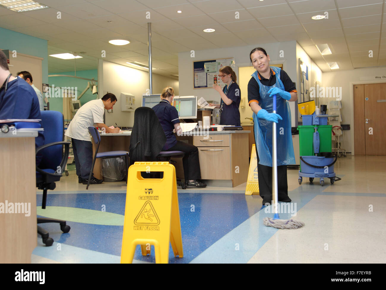 A hospital cleaner mops the floor in the ward administration area in a modern UK hospital. Wet
