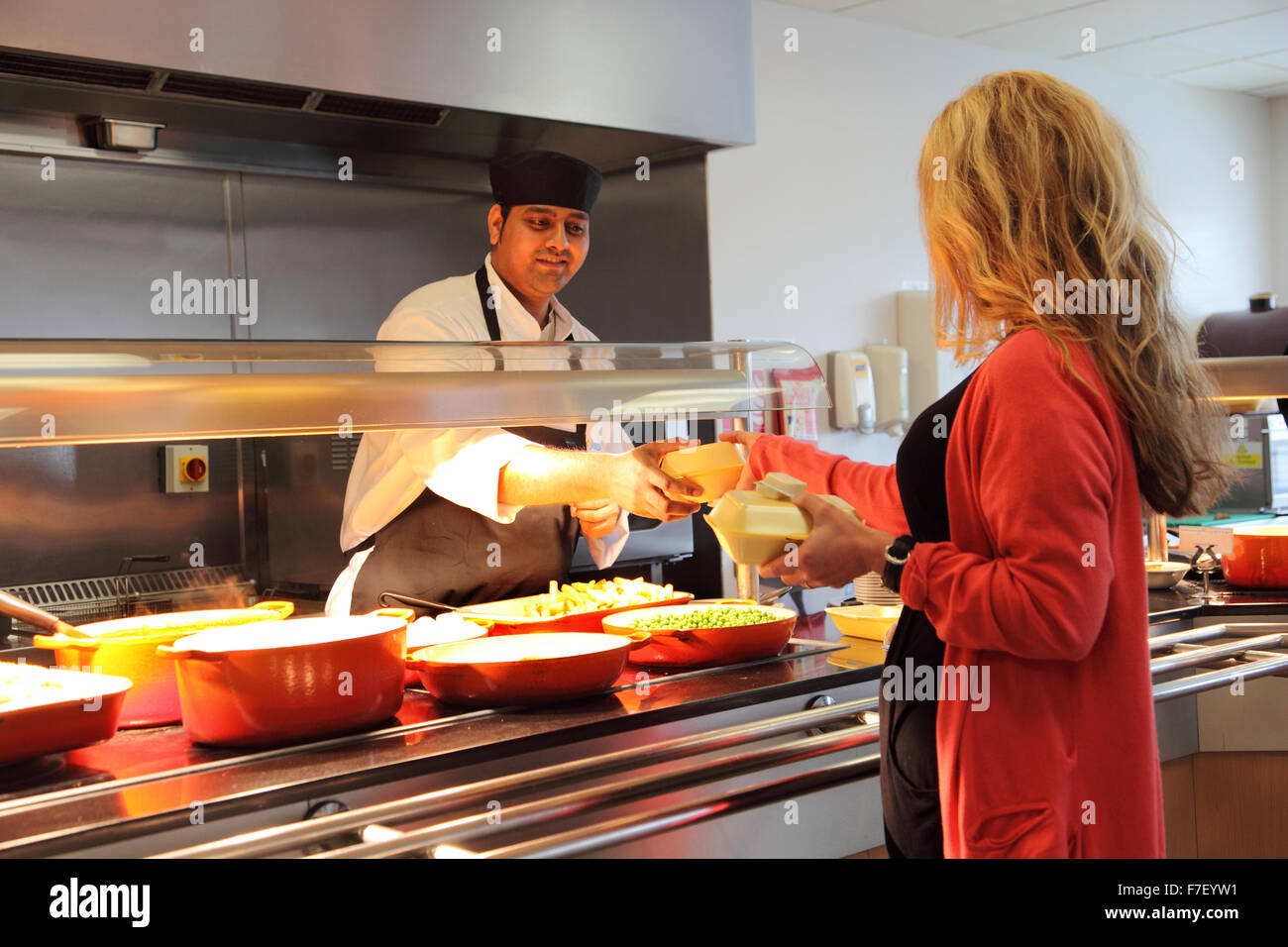 A member of canteen staff hand a customer food in take-away containers in a modern office canteen Stock Photo