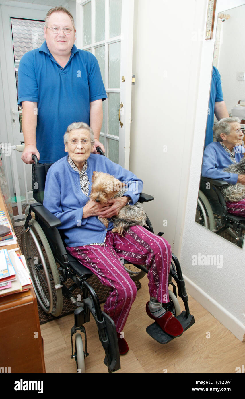 Male carer pushing an elderly woman in a wheelchair (could be mother & son) Stock Photo