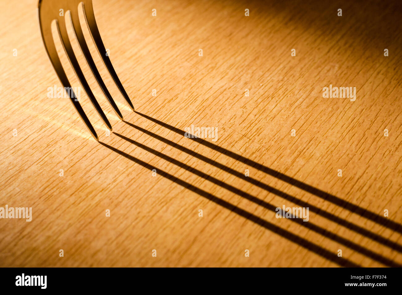 Single kitchen fork creates long shadows on a wooden work surface Stock Photo