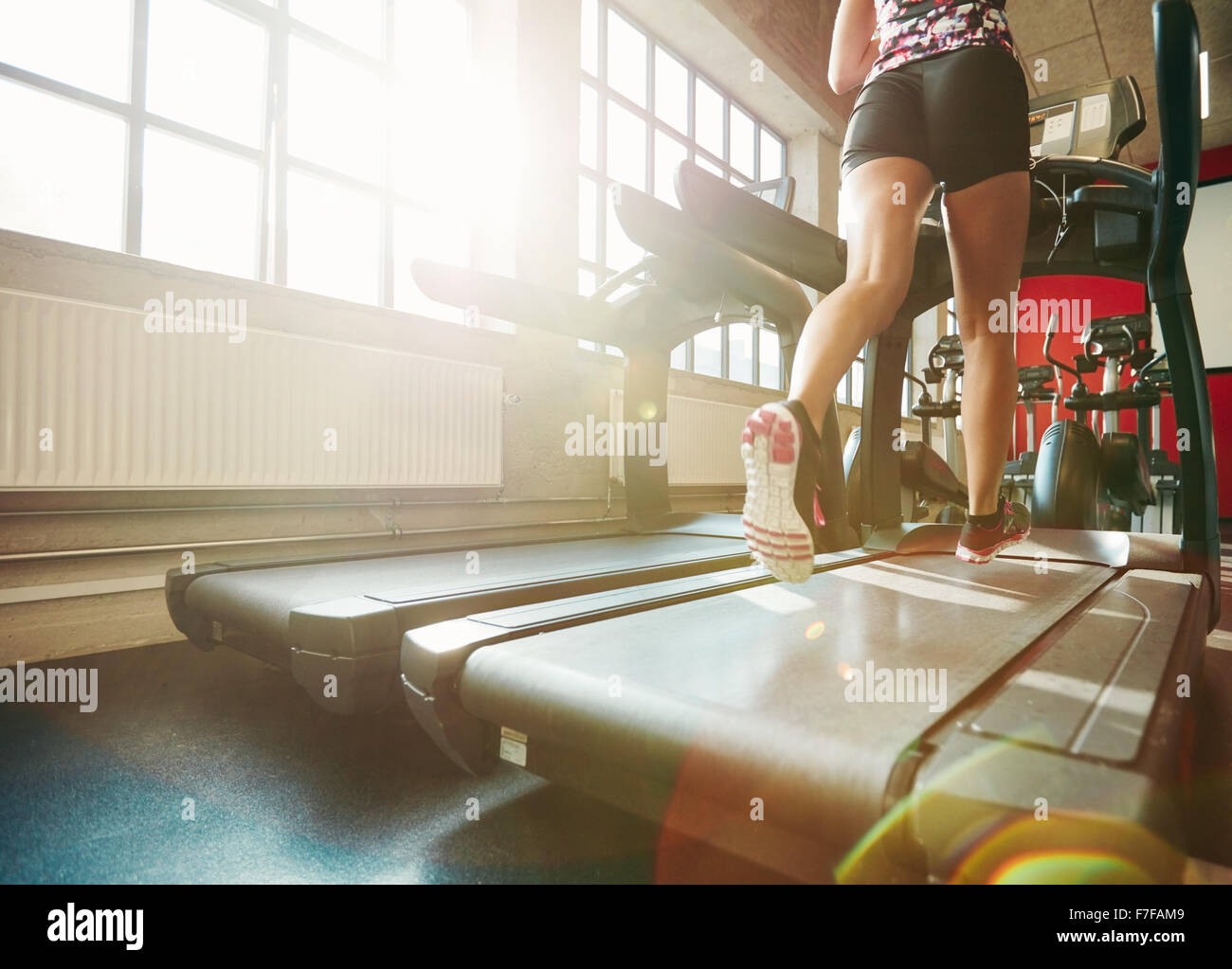 Rear view of woman in action running on treadmill. Focus on woman legs exercising on treadmill at the gym. Stock Photo