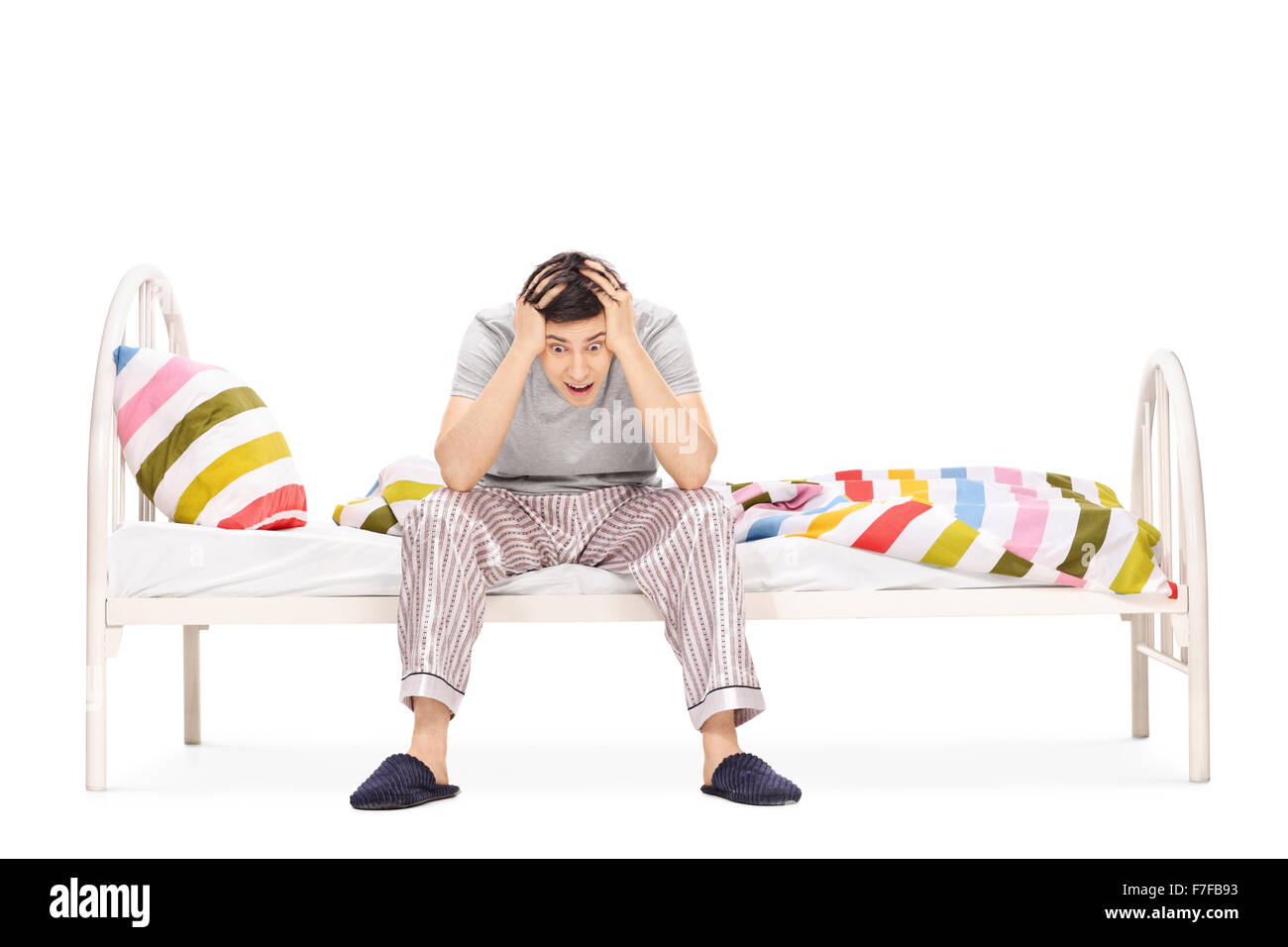 Young guy in pajamas sitting on a bed and suffering from insomnia isolated on white background Stock Photo