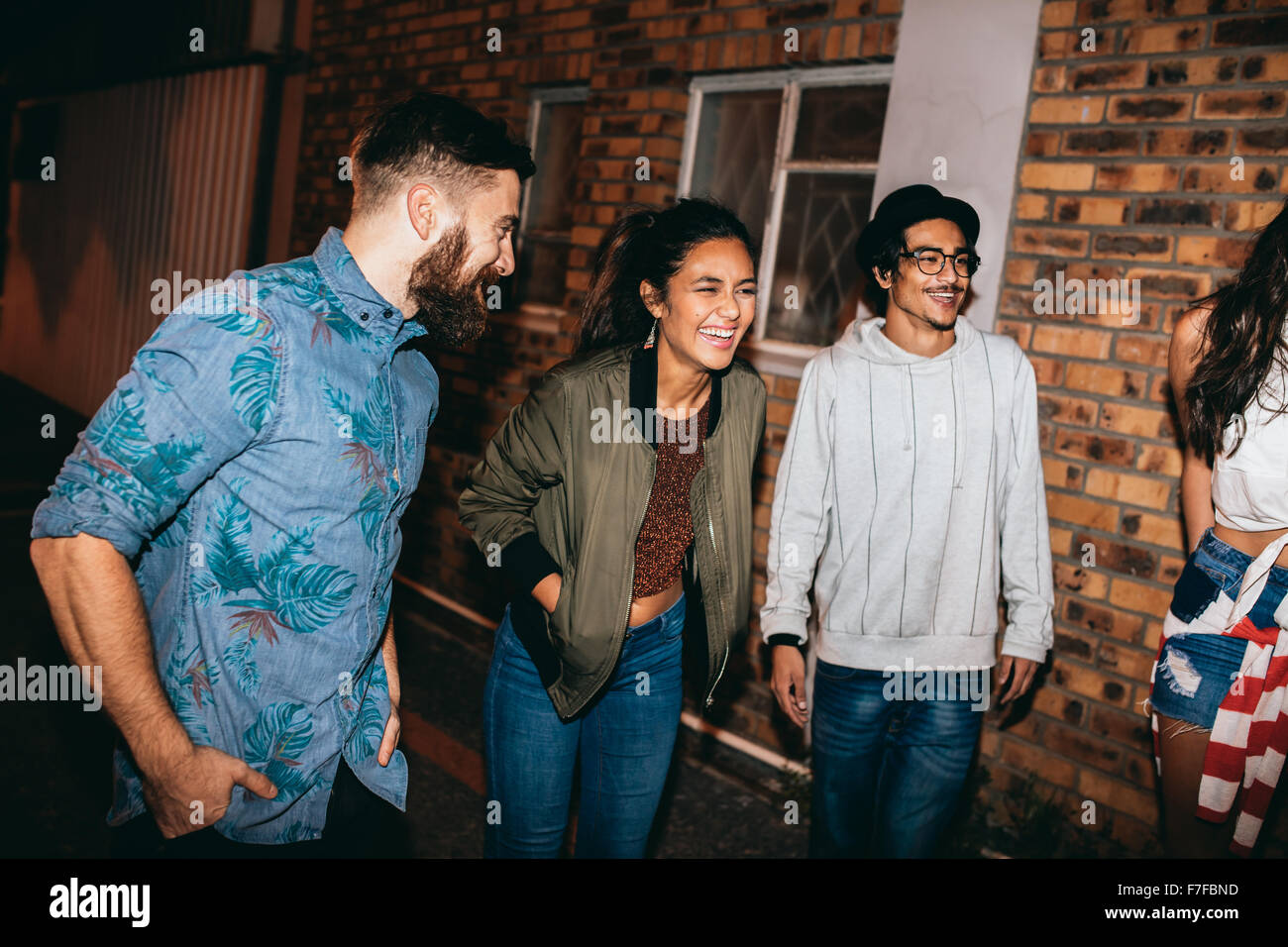 Multi-ethnic group of friends chatting and laughing at the party. Young men and women hanging out together at rooftop party. Stock Photo