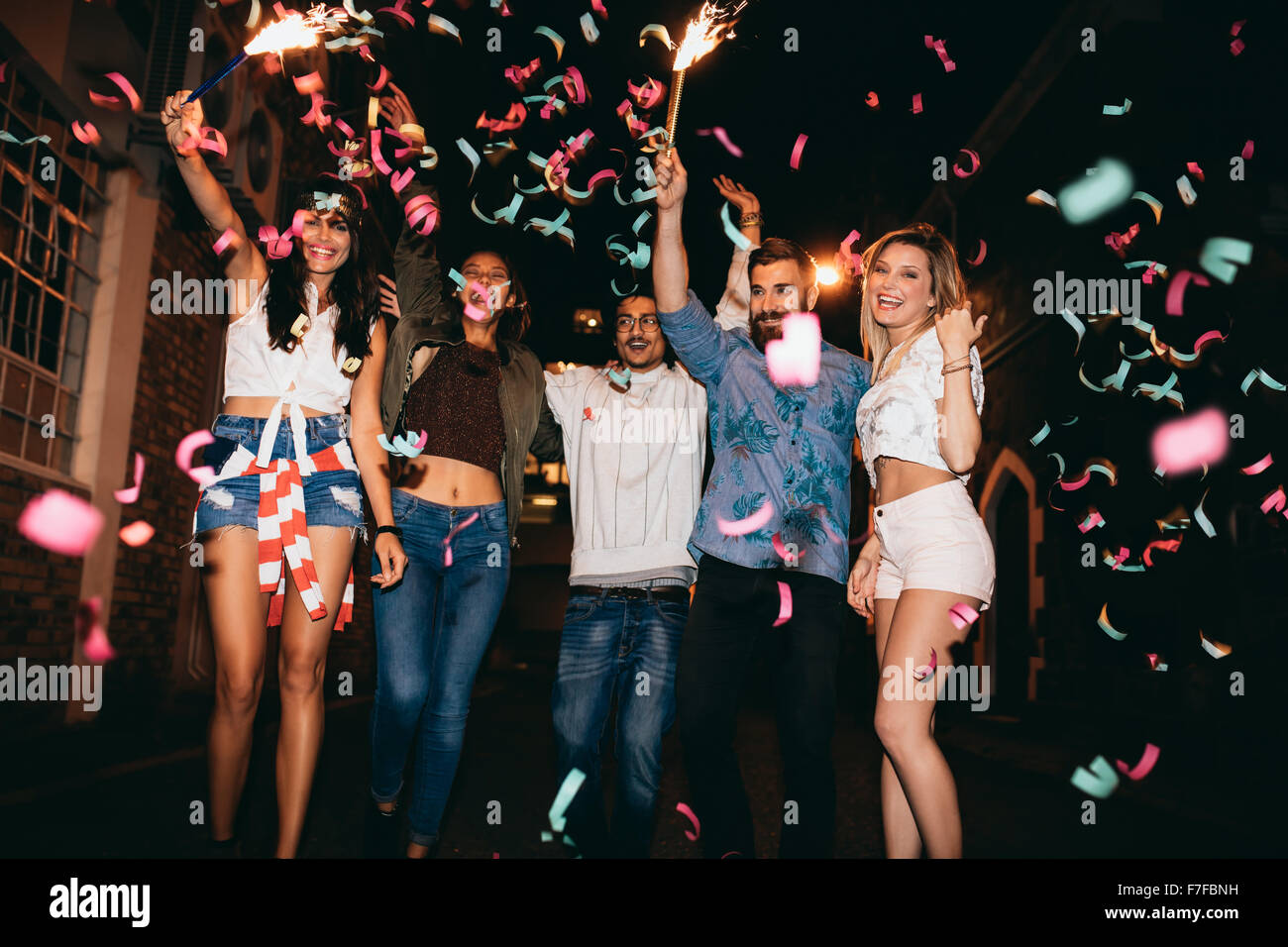 Group of young people having a party, outdoors. Multiracial young men and women celebrating with confetti. Best friend having pa Stock Photo