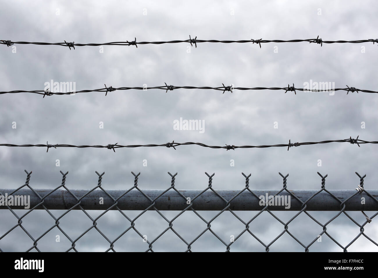 A view of the sky with dark clouds behind a barbed wire security fence ...