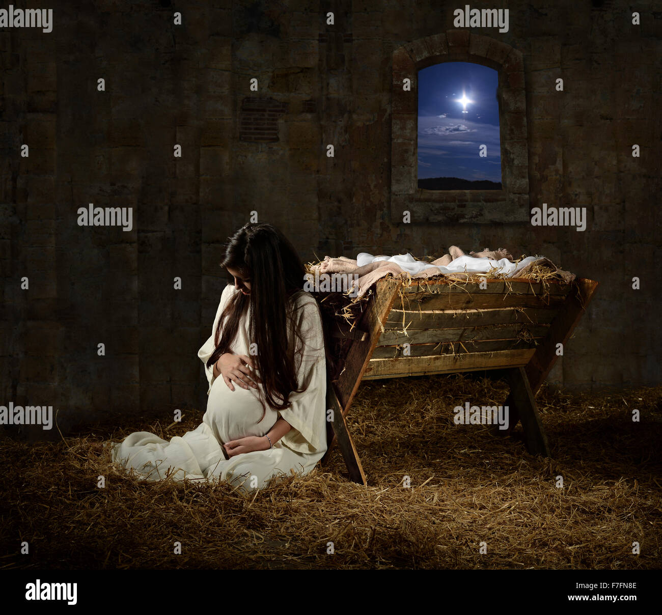 Young pregnant Mary praying leaning on manger on Christmas Eve Stock Photo
