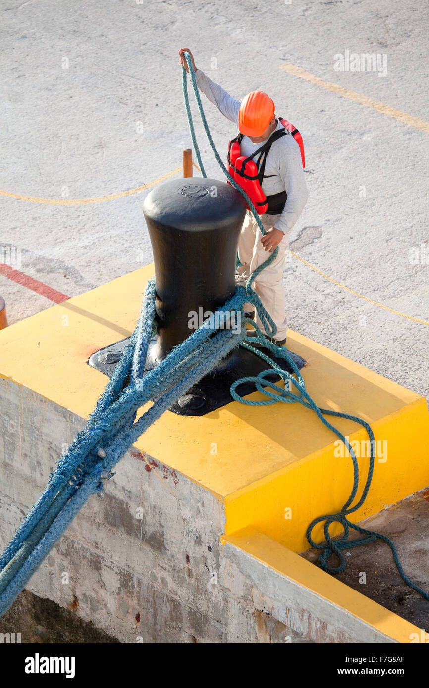 A Mexican dockworker ties cruise ship mooring lines to a large bollard attached to a dock in Cancun, Mexico. Stock Photo
