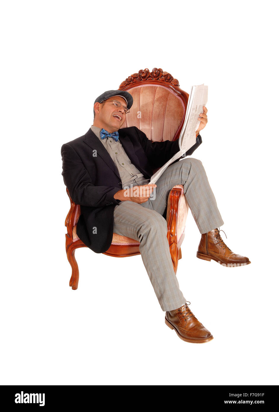 A middle age Hispanic man sitting in a armchair reading his newspaper, laughing what he reads, isolated for white background. Stock Photo
