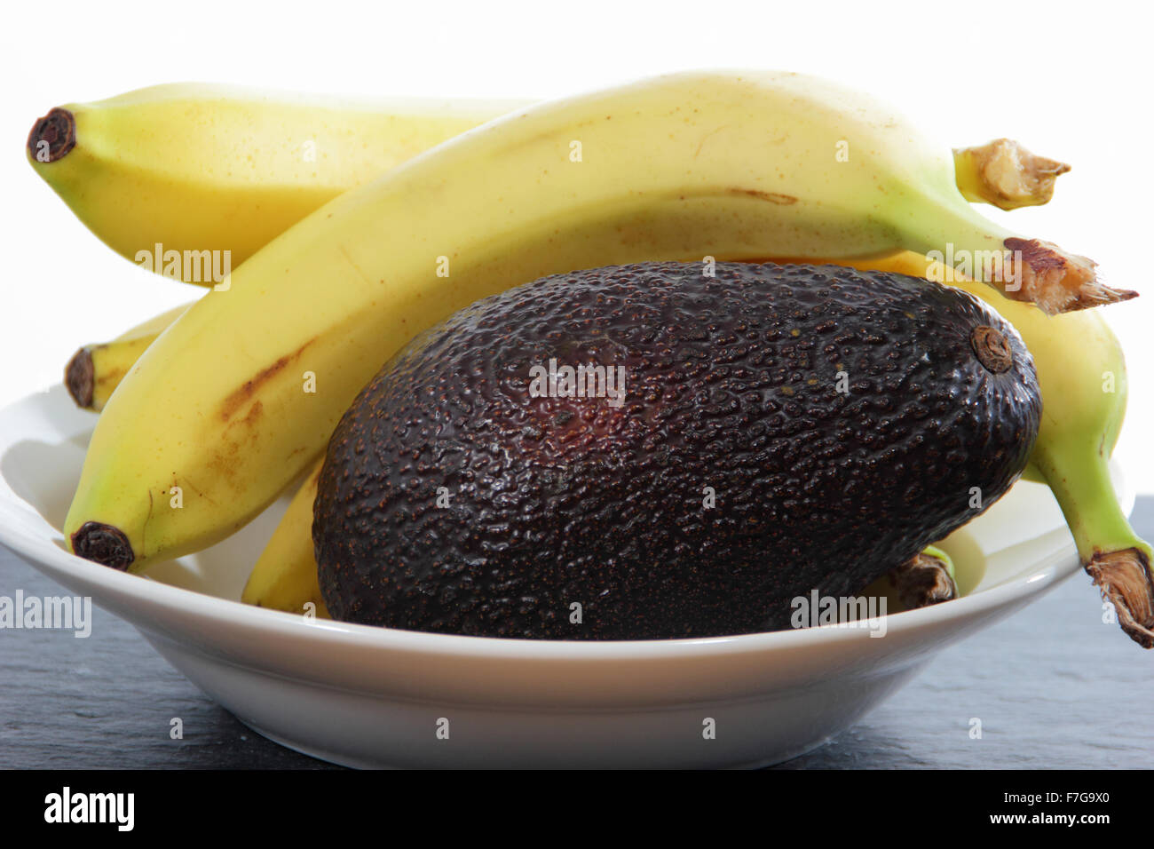 Bananas in a bowl with an avocado to hasten the ripening process - domestic setting , UK Stock Photo