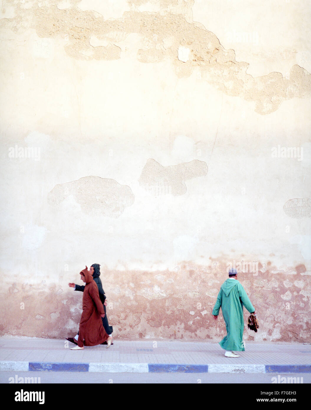 Moroccan muslim men walk briskly past the city walls on his way to morning prayers. Essaouira,Morocco Stock Photo