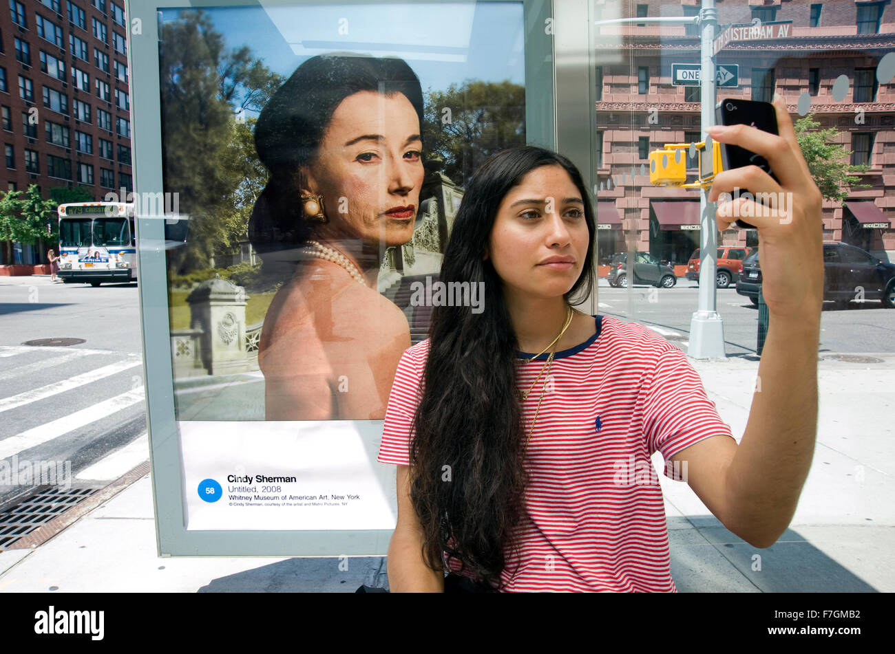 Young woman taking a selfie in front of a Cindy Sherman photograph reproduced on an outdoor advertising panel at a bus shelter in Manhattan for the Art Everywhere project. Stock Photo