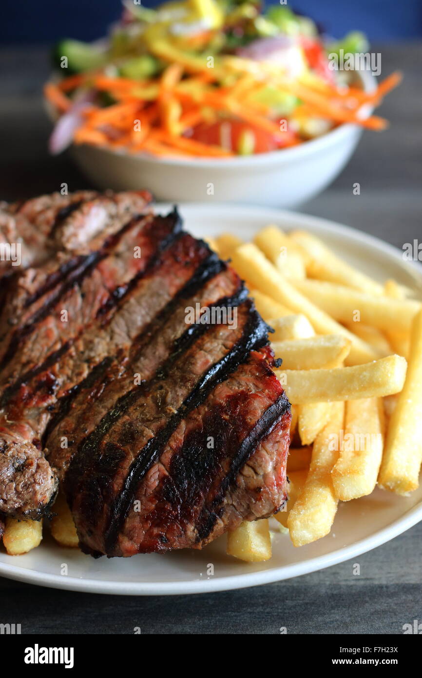 A plate of steak and chips with a bowl of Greek salad in the background Stock Photo Alamy