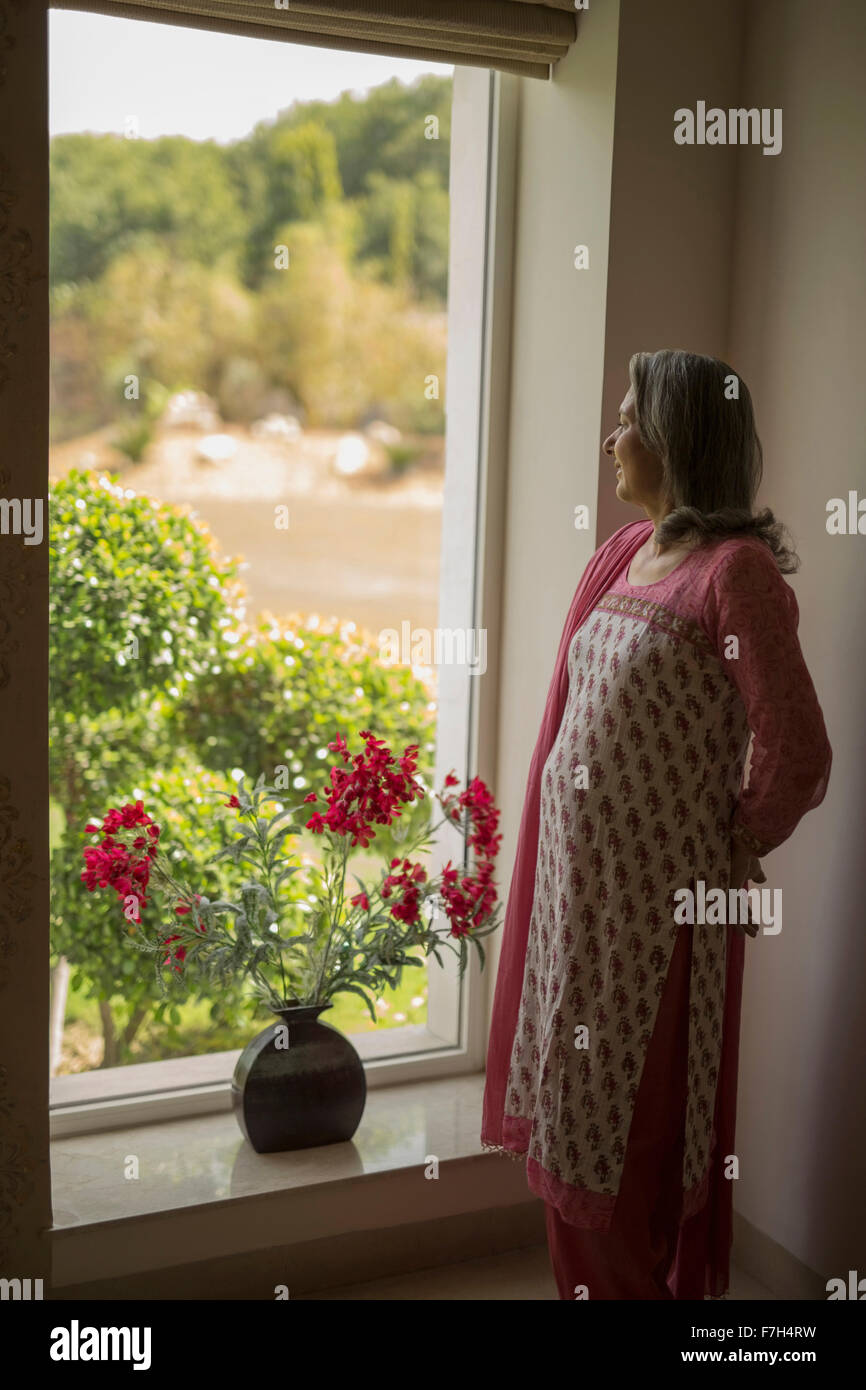 Mature woman, hands behind back looking out window Stock Photo