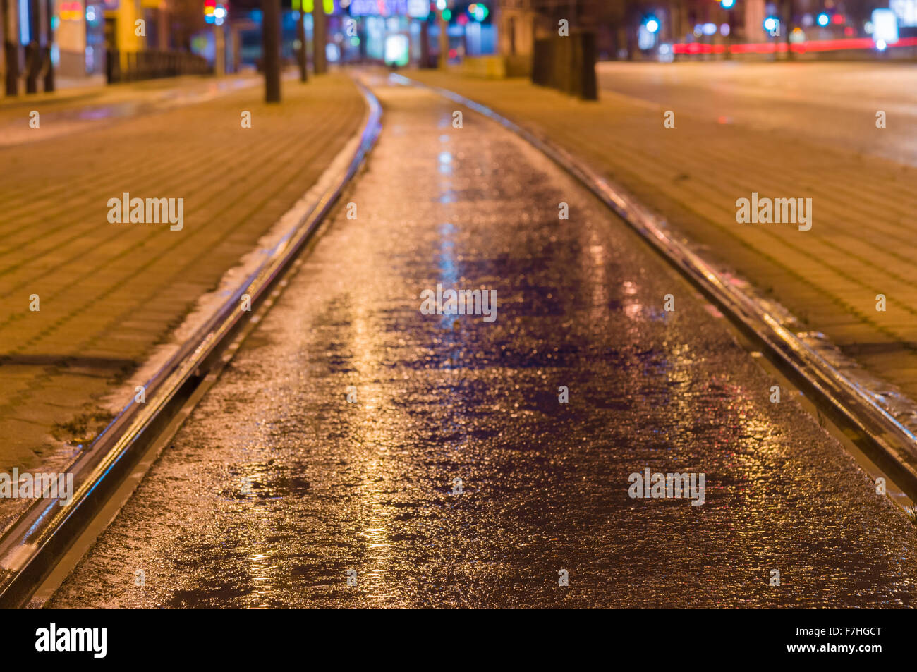Tram rail track wet and shiny by night lights, blurred city background Stock Photo