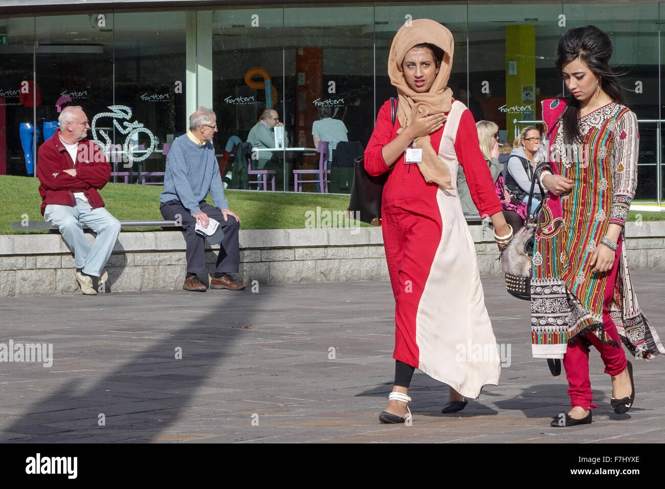 Two Muslim women walking in Bradford Centenary Square wearing traditional eastern clothing with two elderly men in the background Stock Photo
