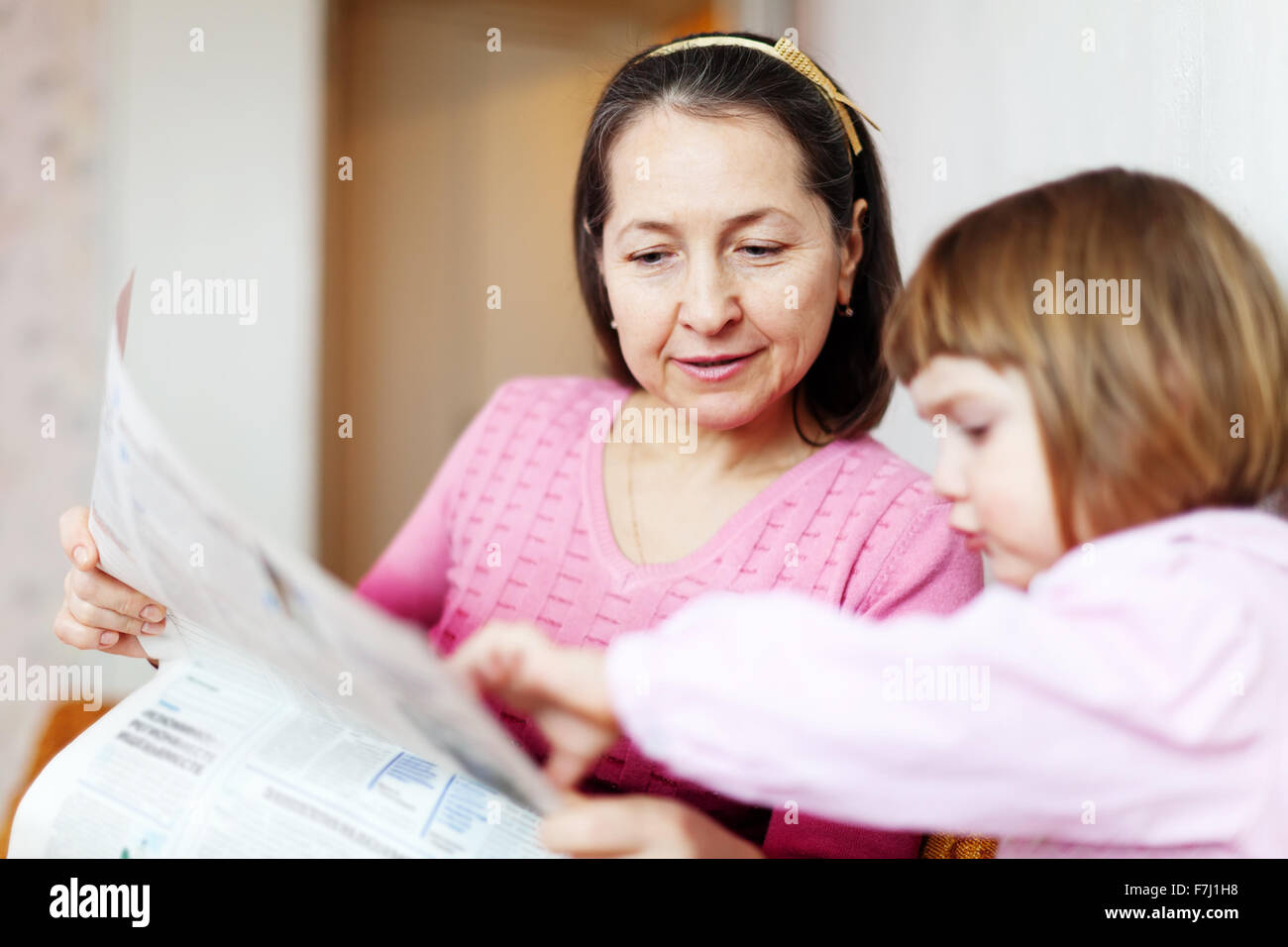 Mature grandmother and child reading newspaper at home Stock Photo - Alamy