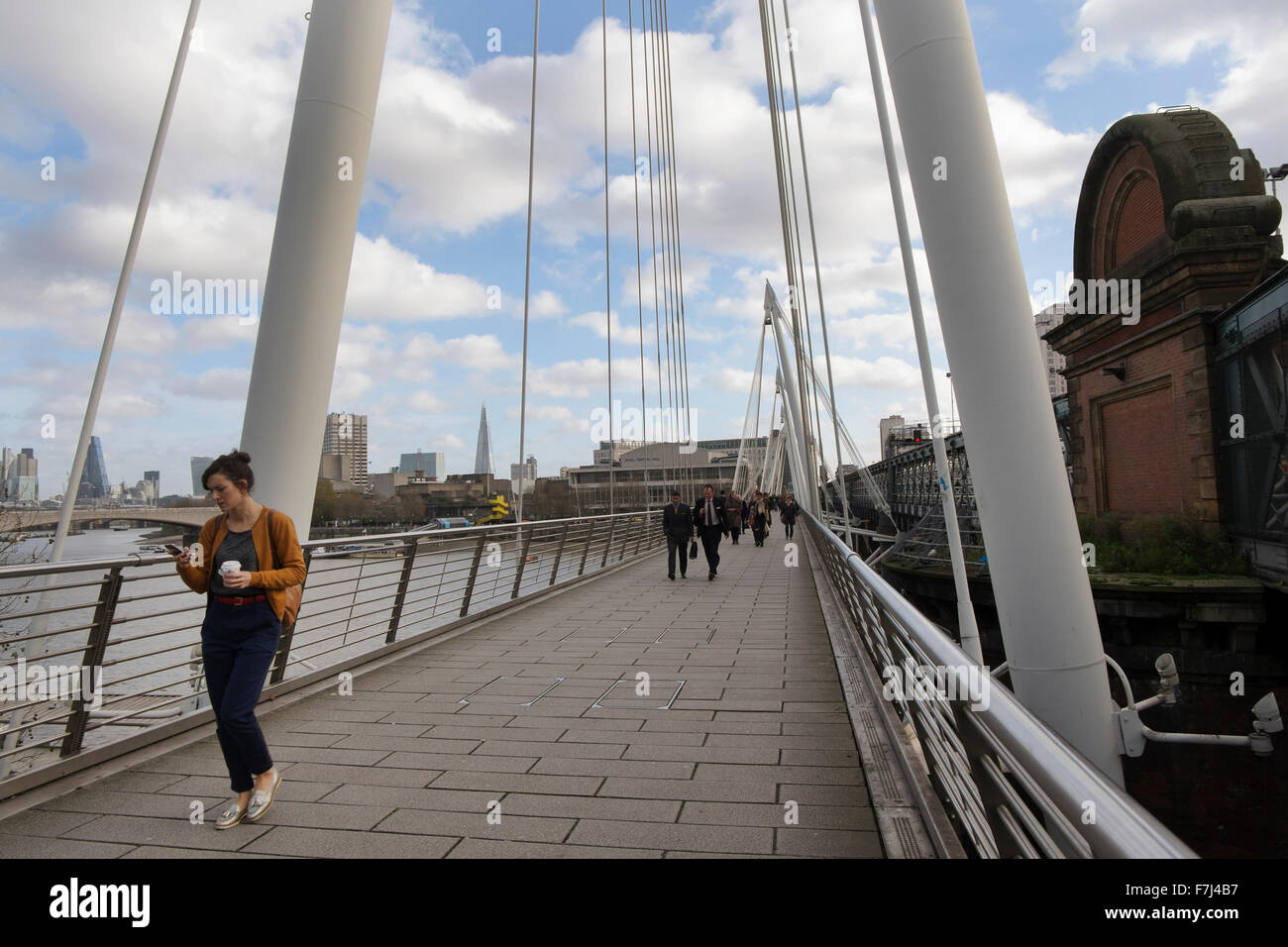 A woman looking at her smart phone walking across one of the Golden Jubilee foot bridges over the River Thames, London, UK Stock Photo