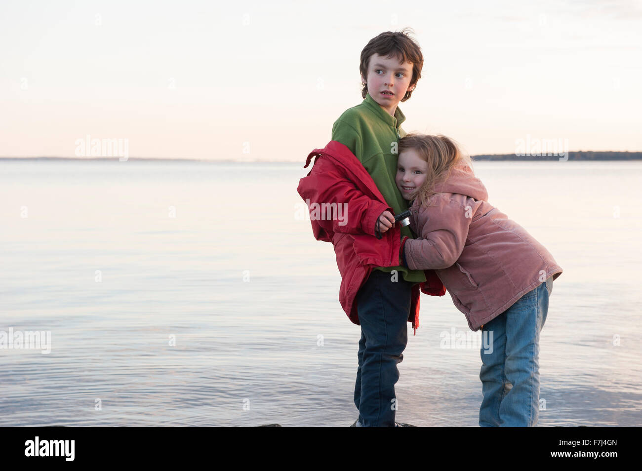 Little girl hugging her brother at water's edge Stock Photo